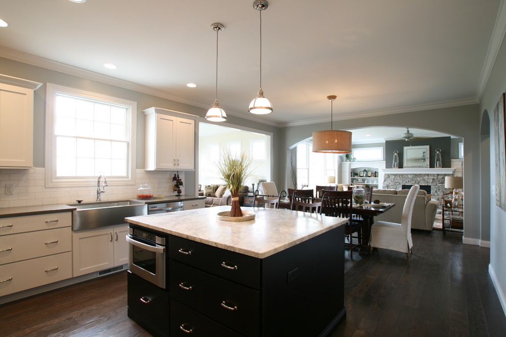 Traditional l-shaped eat-in kitchen in Chicago with a farmhouse sink, flat-panel cabinets, dark wood cabinets, marble benchtops, white splashback, subway tile splashback and stainless steel appliances.