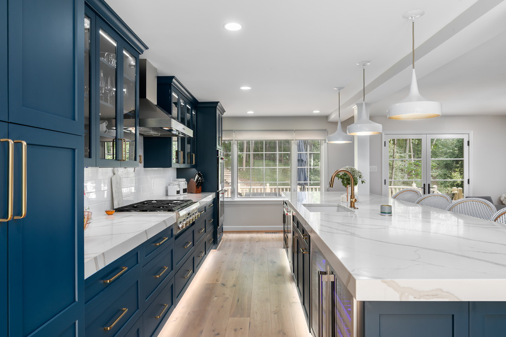 Photo of an expansive contemporary single-wall eat-in kitchen in DC Metro with an undermount sink, glass-front cabinets, blue cabinets, quartz benchtops, white splashback, ceramic splashback, stainless steel appliances, light hardwood floors, with island, beige floor and white benchtop.