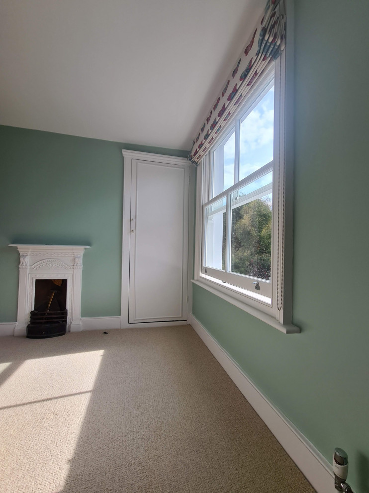 This is an example of a mid-sized traditional guest bedroom in London with green walls, carpet, a standard fireplace, a metal fireplace surround, beige floor and recessed.