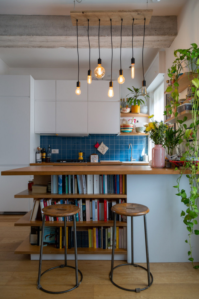 Zweizeilige Moderne Küche mit flächenbündigen Schrankfronten, weißen Schränken, Arbeitsplatte aus Holz, Küchenrückwand in Blau, Elektrogeräten mit Frontblende, braunem Holzboden, Halbinsel, braunem Boden und brauner Arbeitsplatte in Mailand