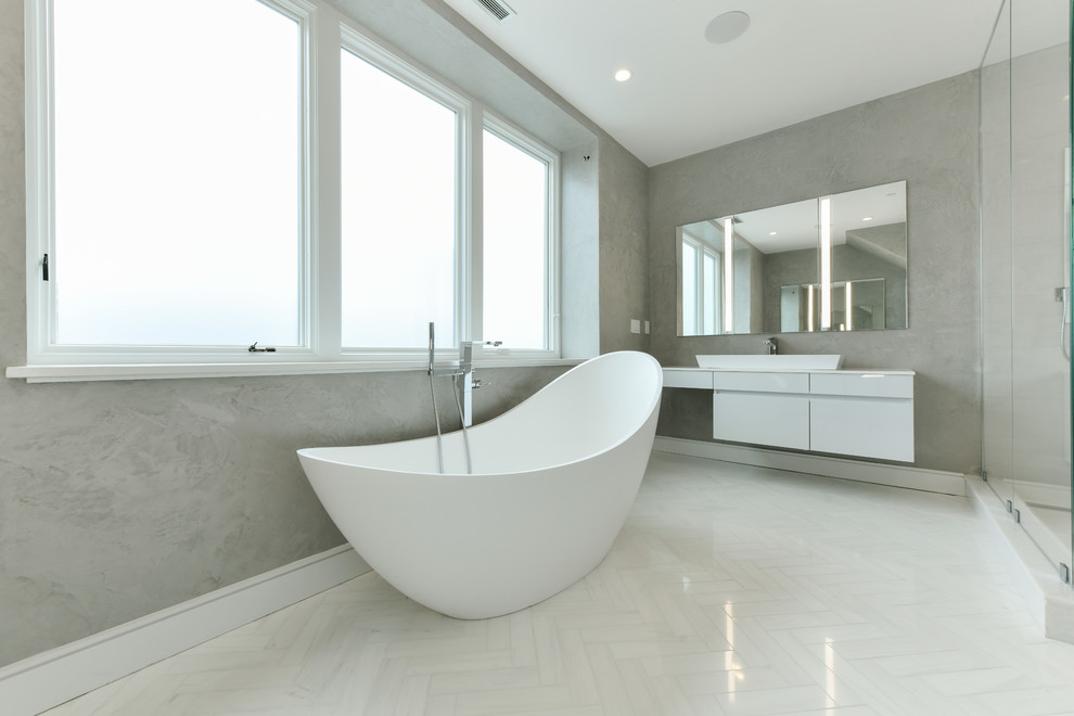 Large modern master bathroom in Boston with flat-panel cabinets, white cabinets, a freestanding tub, a double shower, white tile, porcelain tile, grey walls, porcelain floors, a vessel sink, white floor and a hinged shower door.