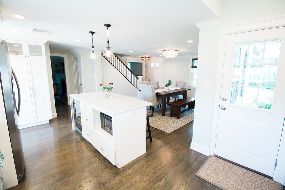 Example of a mid-sized transitional l-shaped dark wood floor and brown floor eat-in kitchen design in Boston with a farmhouse sink, shaker cabinets, white cabinets, marble countertops, gray backsplash, subway tile backsplash, stainless steel appliances and an island