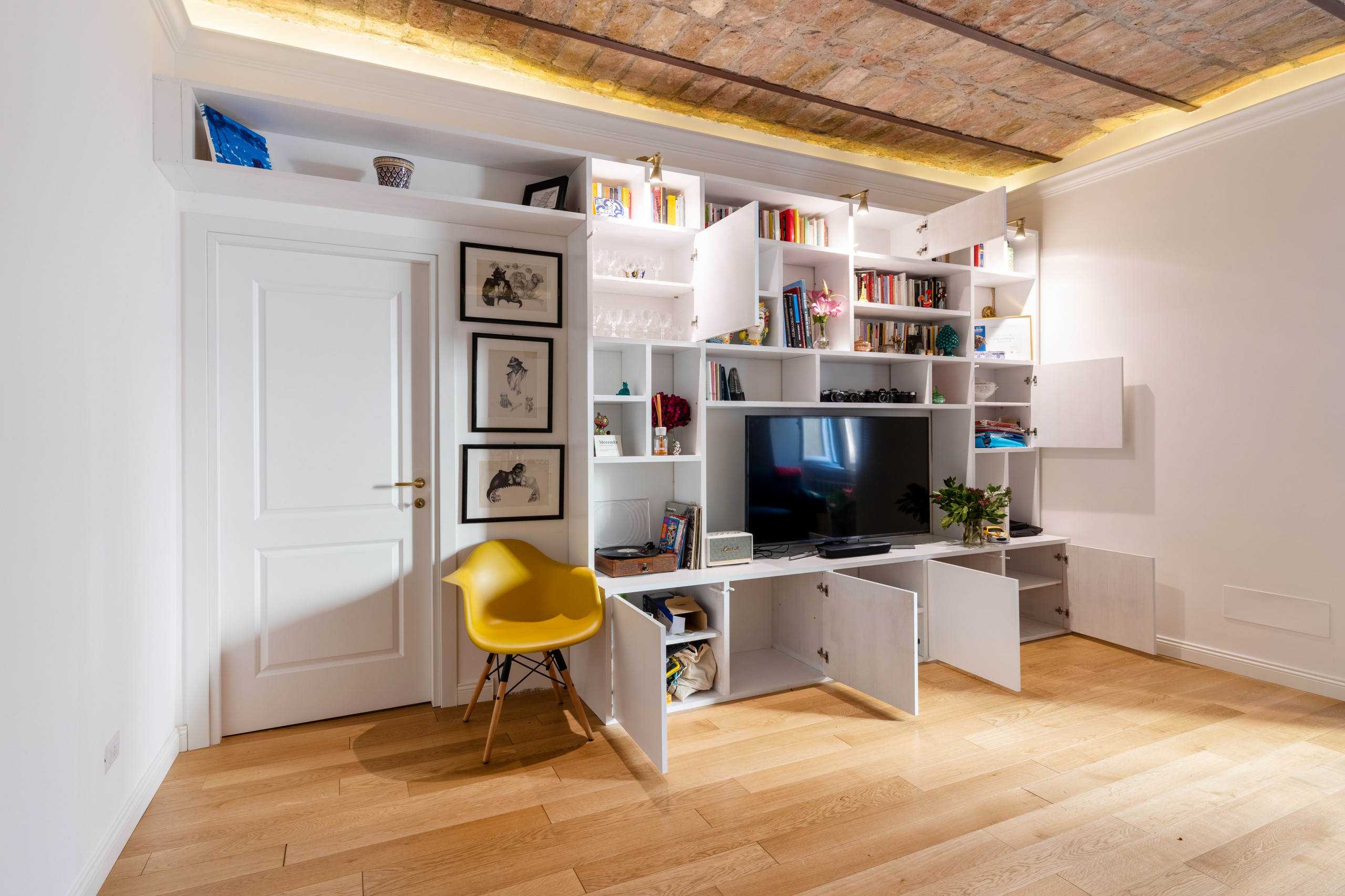 Design arredo su misura, libreria occupa intero muro, integrando le porte già esistenti. Insieme con arredo è stato  progettato la luce adatta allo spazio. Una parete attrezzata per la tv con i conten