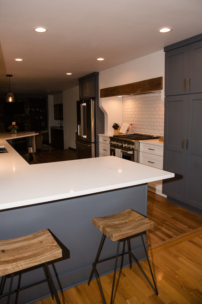 Eat-in kitchen - mid-sized transitional galley medium tone wood floor and white floor eat-in kitchen idea with an undermount sink, shaker cabinets, white cabinets, solid surface countertops, white backsplash, ceramic backsplash, stainless steel appliances, a peninsula and white countertops