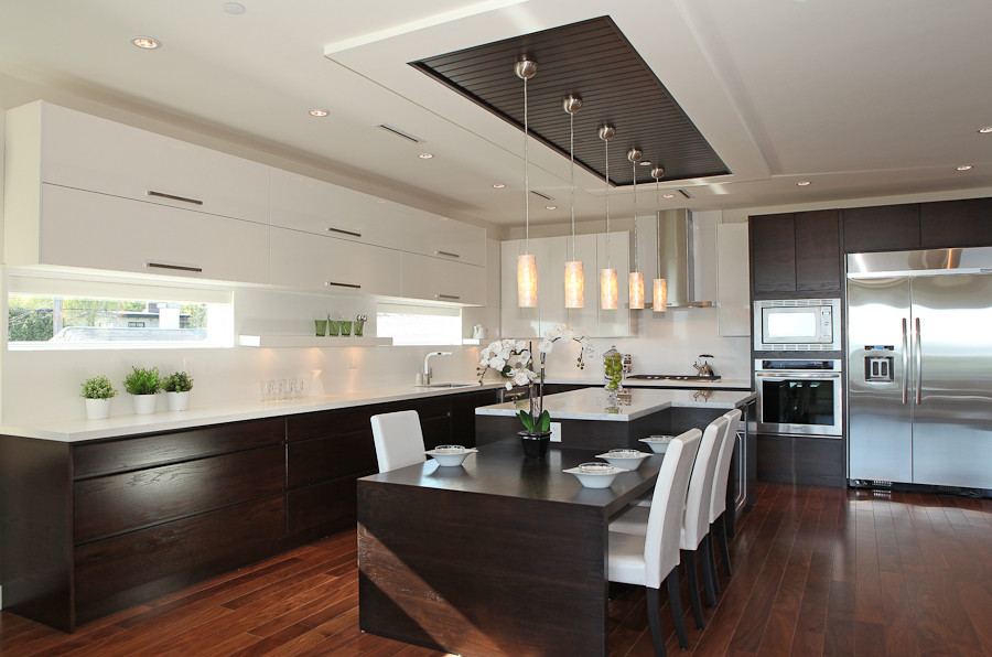 Photo of a large contemporary l-shaped open plan kitchen in Vancouver with a drop-in sink, flat-panel cabinets, dark wood cabinets, marble benchtops, white splashback, stone slab splashback, stainless steel appliances and with island.