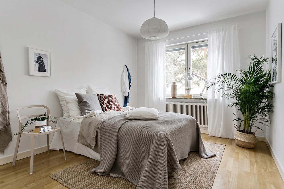 This is an example of a scandinavian bedroom in Stockholm with white walls, light hardwood floors and beige floor.