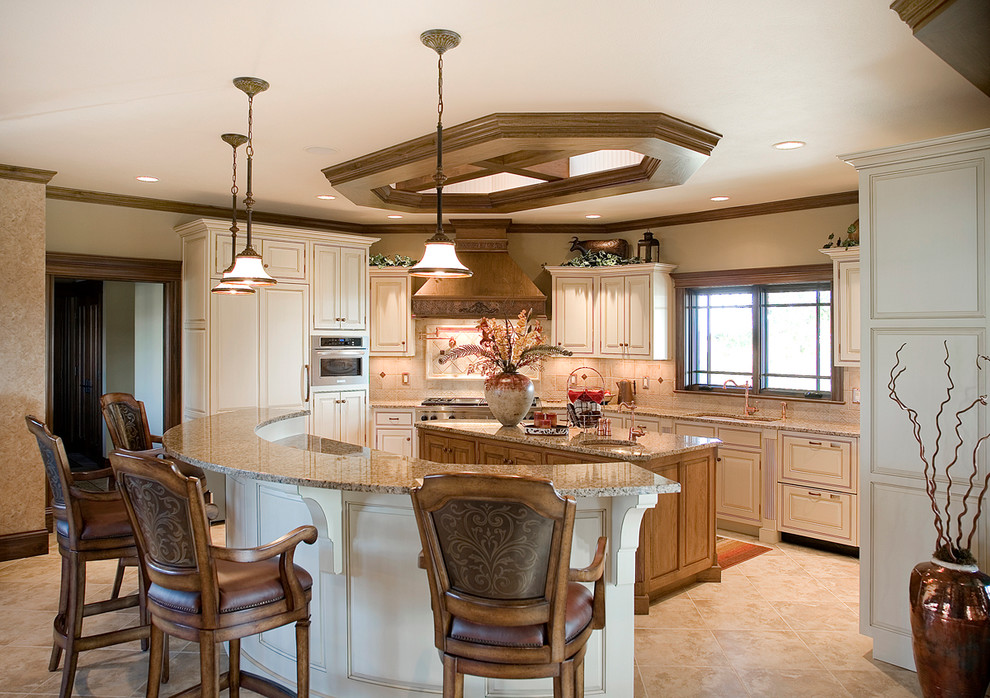 Photo of a large traditional u-shaped eat-in kitchen in Other with multiple islands, an undermount sink, raised-panel cabinets, granite benchtops, beige splashback, travertine splashback, panelled appliances, porcelain floors, beige floor and beige cabinets.