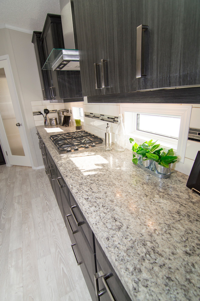 Photo of a mid-sized modern l-shaped eat-in kitchen in Calgary with a double-bowl sink, flat-panel cabinets, black cabinets, white splashback, subway tile splashback, stainless steel appliances, linoleum floors and with island.
