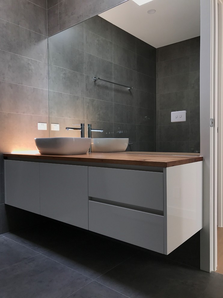 Design ideas for a mid-sized modern kids wet room bathroom in Melbourne with flat-panel cabinets, white cabinets, gray tile, grey walls, a vessel sink and wood benchtops.