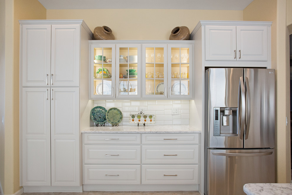 Eat-in kitchen - mid-sized transitional single-wall ceramic tile and beige floor eat-in kitchen idea with an undermount sink, raised-panel cabinets, white cabinets, quartz countertops, white backsplash, porcelain backsplash, stainless steel appliances and an island