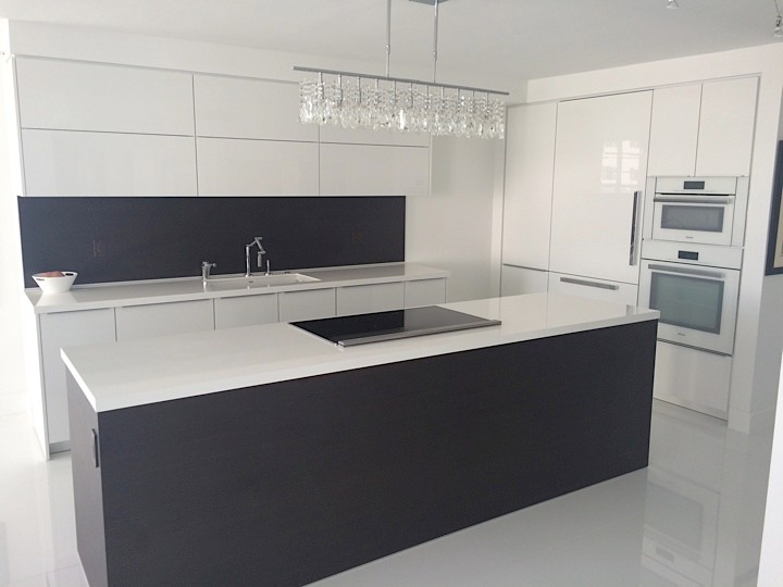 Mid-sized contemporary single-wall open plan kitchen in Boston with an undermount sink, flat-panel cabinets, white cabinets, solid surface benchtops, black splashback, panelled appliances, concrete floors, with island and white floor.