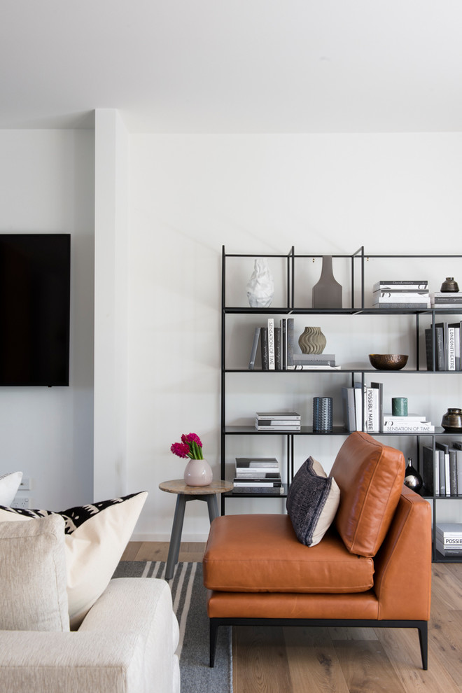 Mid-sized midcentury open concept living room in Melbourne with white walls, light hardwood floors, no fireplace, a metal fireplace surround, a wall-mounted tv and brown floor.