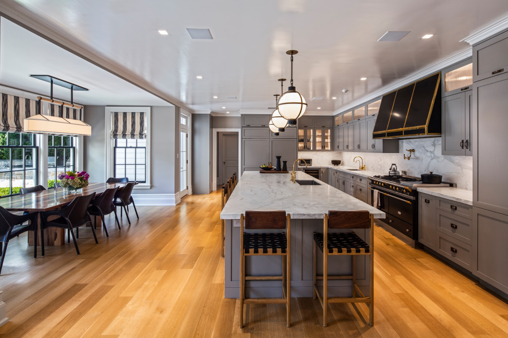 Inspiration for a large traditional l-shaped eat-in kitchen in New York with an undermount sink, shaker cabinets, grey cabinets, marble benchtops, white splashback, marble splashback, black appliances, with island, white benchtop, medium hardwood floors and brown floor.
