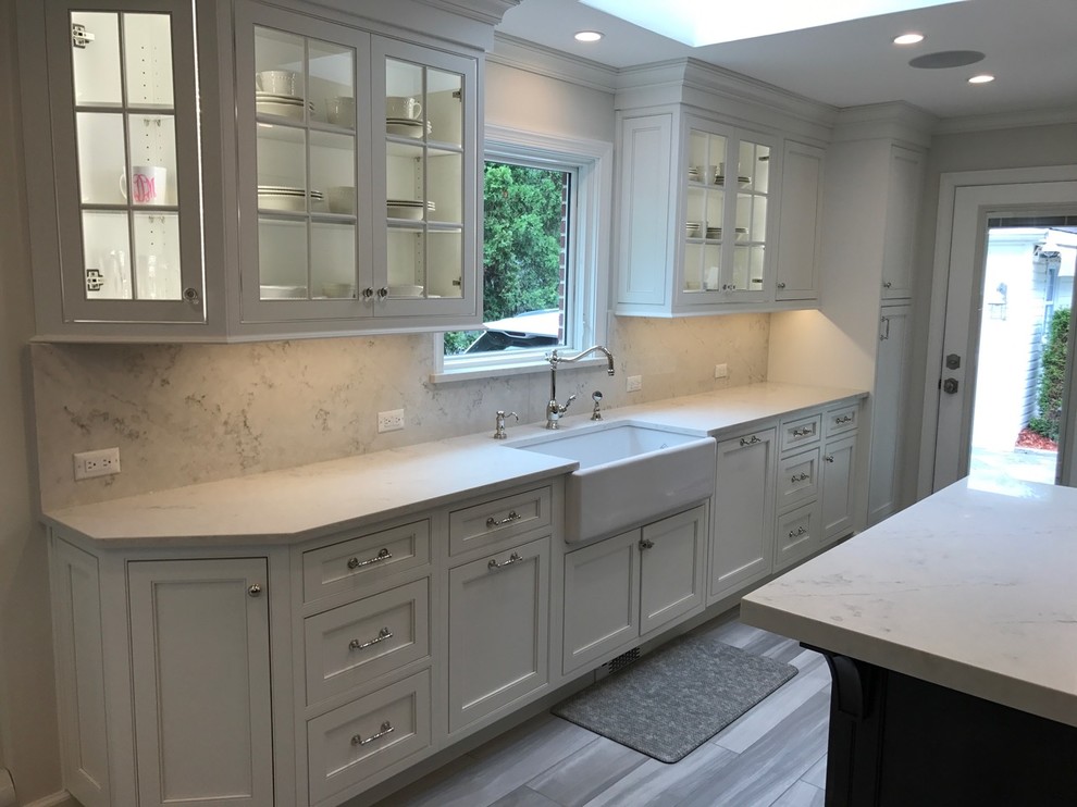 Inspiration for a mid-sized transitional u-shaped light wood floor and brown floor open concept kitchen remodel with a farmhouse sink, recessed-panel cabinets, white cabinets, marble countertops, white backsplash, marble backsplash, stainless steel appliances and an island