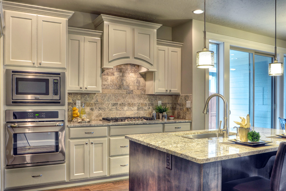 Example of a small transitional l-shaped medium tone wood floor eat-in kitchen design in Boise with an undermount sink, recessed-panel cabinets, white cabinets, granite countertops, beige backsplash, stone tile backsplash, stainless steel appliances and an island