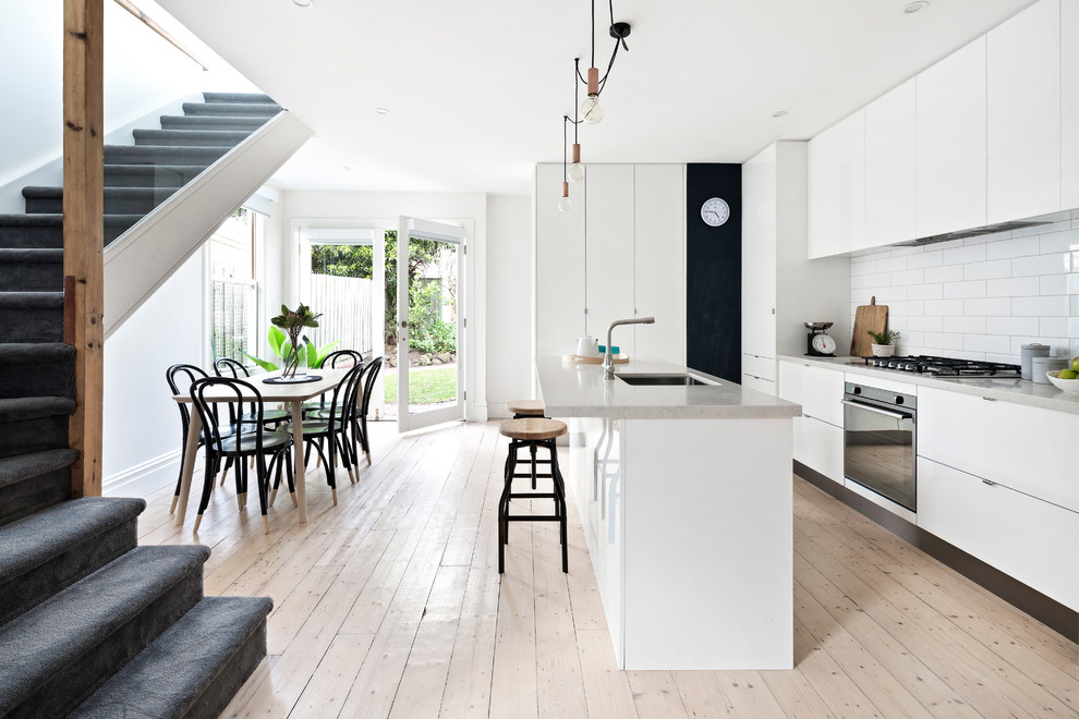Contemporary eat-in kitchen in Melbourne with an undermount sink, flat-panel cabinets, white cabinets, white splashback, light hardwood floors and with island.