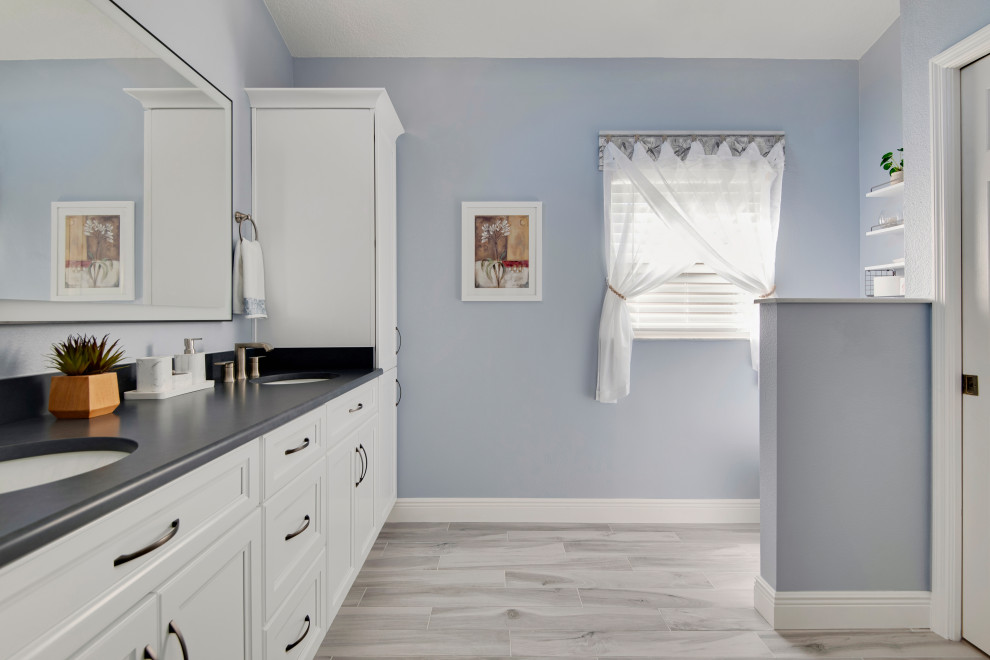 Photo of a large beach style master bathroom in Tampa with shaker cabinets, white cabinets, a corner shower, a two-piece toilet, white tile, porcelain tile, blue walls, ceramic floors, an undermount sink, engineered quartz benchtops, beige floor, a hinged shower door, black benchtops, a double vanity and vaulted.