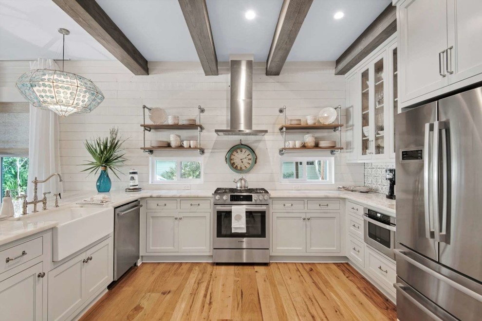 Design ideas for a mid-sized beach style u-shaped separate kitchen in Miami with a farmhouse sink, shaker cabinets, white cabinets, stainless steel appliances, light hardwood floors, a peninsula, brown floor, white benchtop, quartzite benchtops, white splashback and timber splashback.