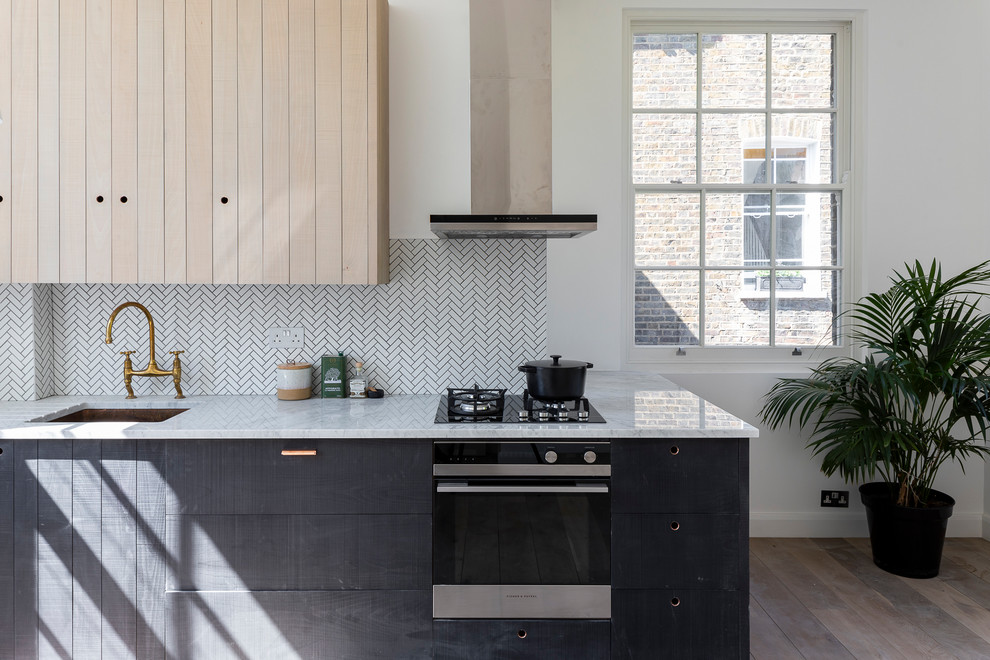 This is an example of a small scandinavian single-wall kitchen in London with an undermount sink, flat-panel cabinets, black cabinets, marble benchtops, white splashback, matchstick tile splashback, black appliances, medium hardwood floors, no island, brown floor and white benchtop.