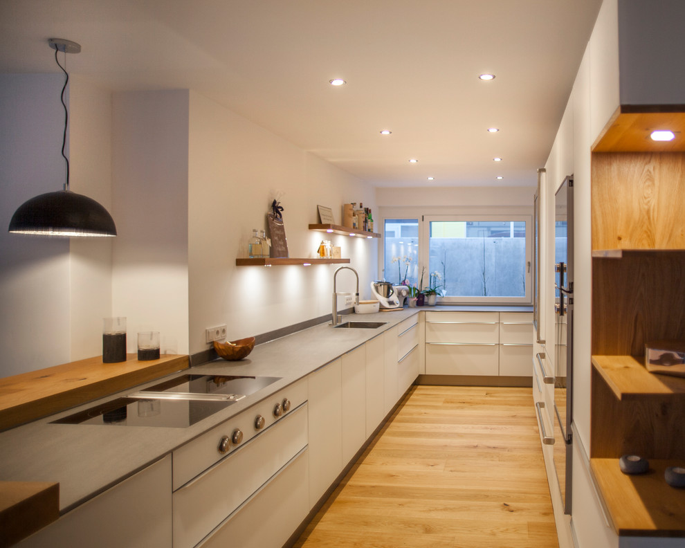 Photo of a contemporary u-shaped separate kitchen in Munich with an integrated sink, flat-panel cabinets, white cabinets, black appliances, light hardwood floors, no island and brown floor.