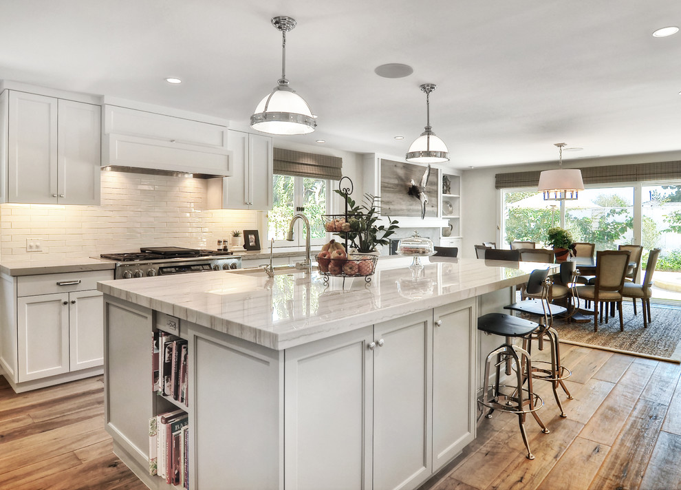 Mid-sized transitional l-shaped medium tone wood floor open concept kitchen photo in Orange County with recessed-panel cabinets, white cabinets, white backsplash, stainless steel appliances, an island, an undermount sink, subway tile backsplash, quartzite countertops and white countertops