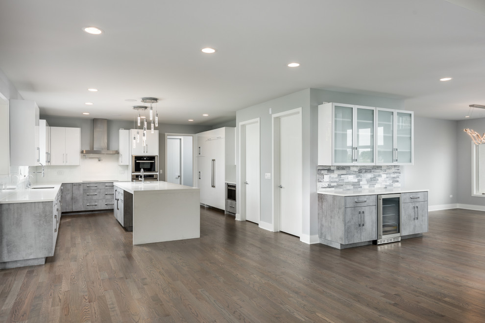 Design ideas for a large modern u-shaped open plan kitchen in Chicago with a single-bowl sink, flat-panel cabinets, white cabinets, quartz benchtops, white splashback, panelled appliances, medium hardwood floors, with island, brown floor, white benchtop and glass tile splashback.