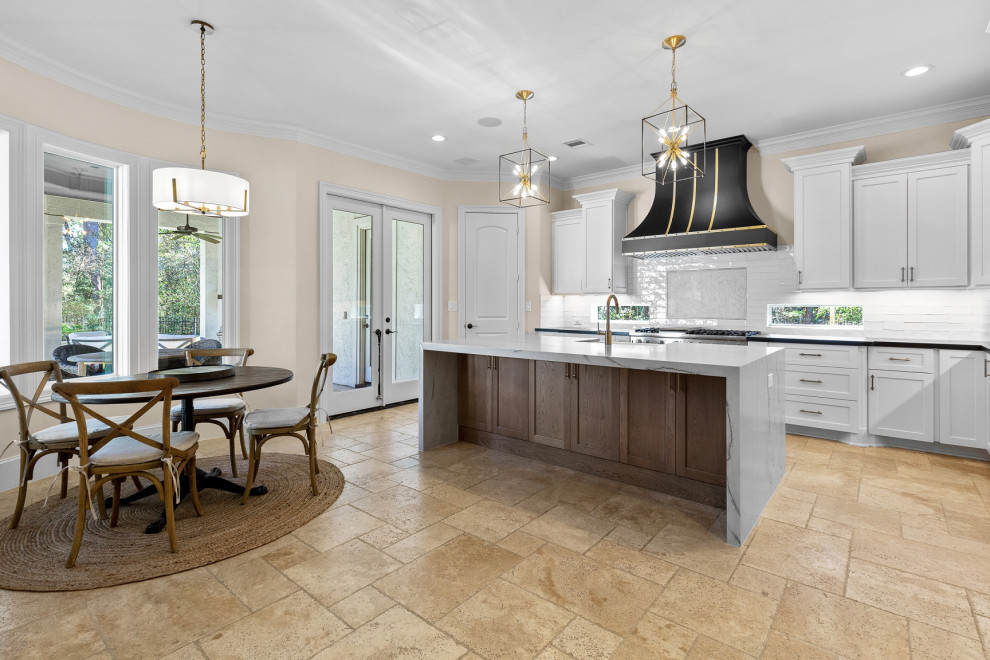 Example of a large transitional l-shaped limestone floor and beige floor eat-in kitchen design in Houston with a farmhouse sink, recessed-panel cabinets, white cabinets, quartzite countertops, white backsplash, limestone backsplash, stainless steel appliances, an island and white countertops
