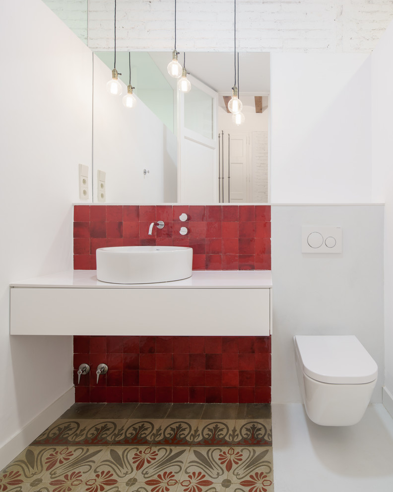 This is an example of a mid-sized mediterranean powder room in Barcelona with flat-panel cabinets, white cabinets, a wall-mount toilet, red tile, white walls, a vessel sink, mosaic tile and multi-coloured floor.