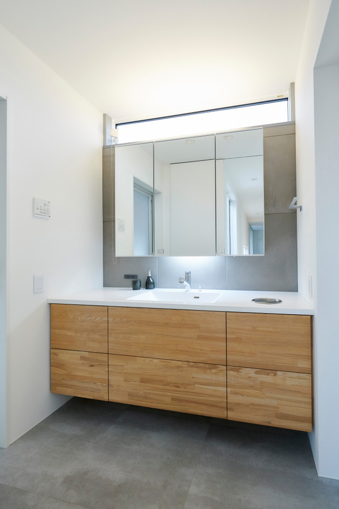 Moderne Gästetoilette mit weißen Schränken, grauen Fliesen, weißer Wandfarbe, grauem Boden und brauner Waschtischplatte in Sonstige