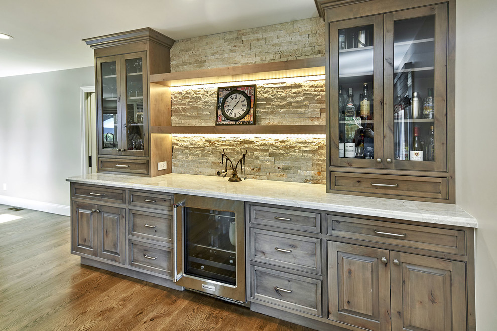 Photo of a mid-sized country single-wall home bar in San Francisco with beaded inset cabinets, grey cabinets, quartzite benchtops, beige splashback, stone tile splashback, medium hardwood floors, brown floor and white benchtop.