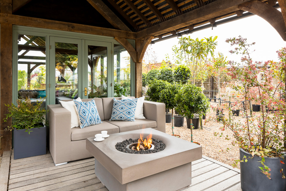 This is an example of a mid-sized country deck in Surrey with a fire feature and a roof extension.