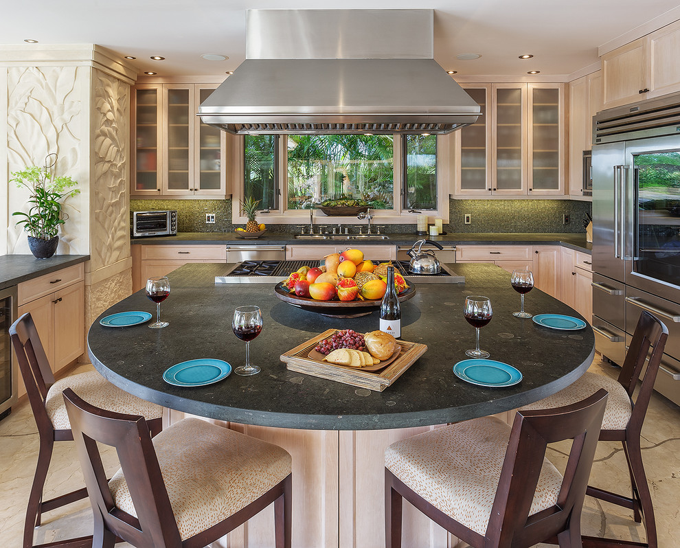 This is an example of a large tropical u-shaped kitchen in Hawaii with a drop-in sink, glass-front cabinets, light wood cabinets, concrete benchtops, multi-coloured splashback, glass tile splashback, stainless steel appliances, limestone floors and with island.