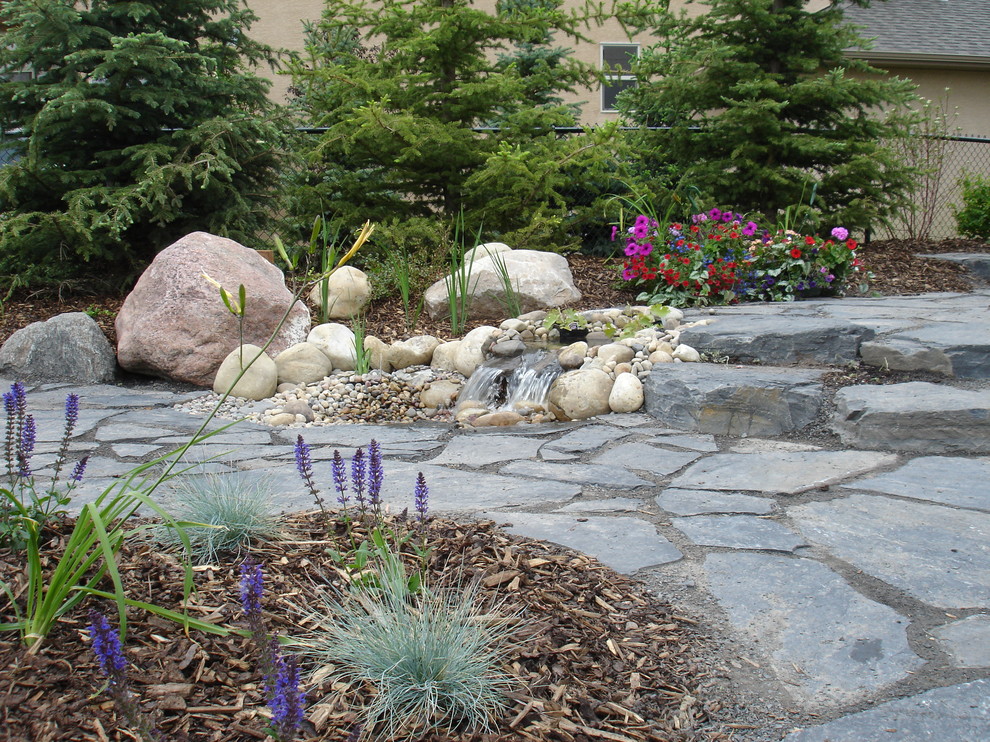 Inspiration for a mid-sized arts and crafts backyard full sun formal garden in Calgary with a water feature and natural stone pavers.