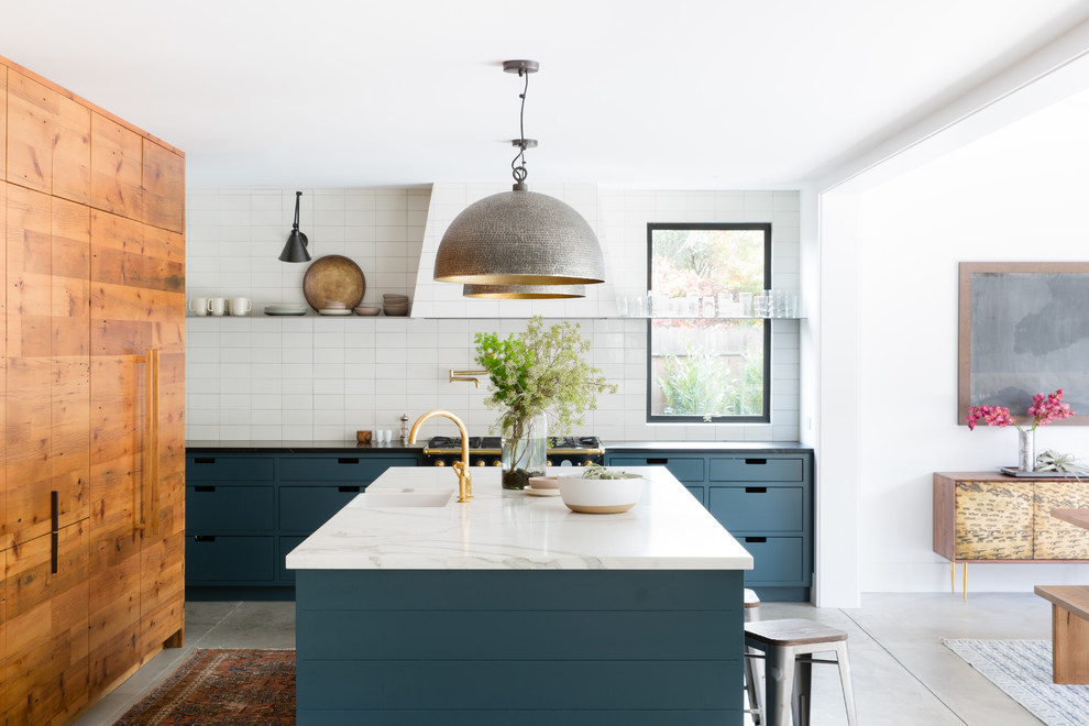 This is an example of a country eat-in kitchen in San Francisco with a farmhouse sink, flat-panel cabinets, blue cabinets, white splashback, black appliances, concrete floors and with island.