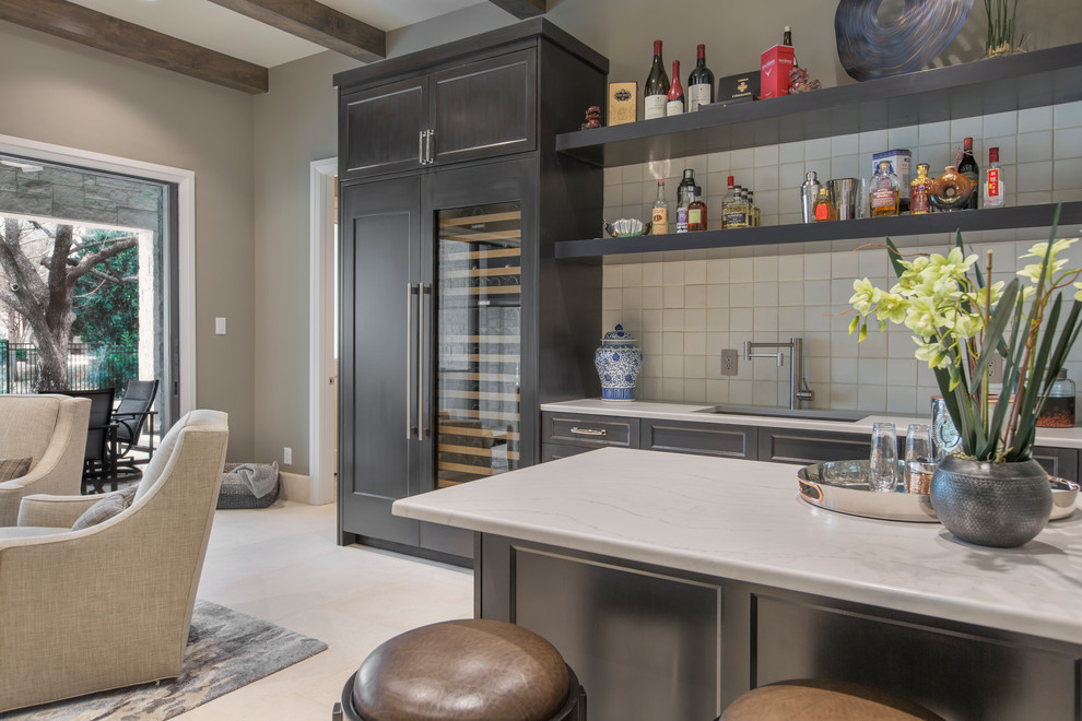 This is an example of a transitional seated home bar in Dallas with recessed-panel cabinets, quartz benchtops, beige splashback, ceramic splashback, limestone floors, beige floor and white benchtop.