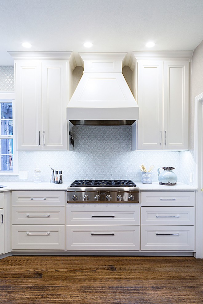 Example of a mid-sized transitional dark wood floor kitchen design in Dallas with a double-bowl sink, blue backsplash, glass sheet backsplash, stainless steel appliances, recessed-panel cabinets, white cabinets, quartzite countertops and an island