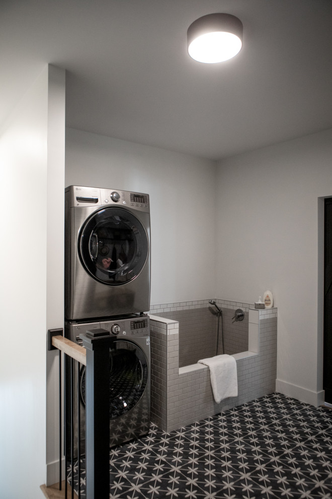 Large scandinavian utility room in Other with shaker cabinets, black cabinets, grey walls, ceramic floors, a stacked washer and dryer and grey floor.