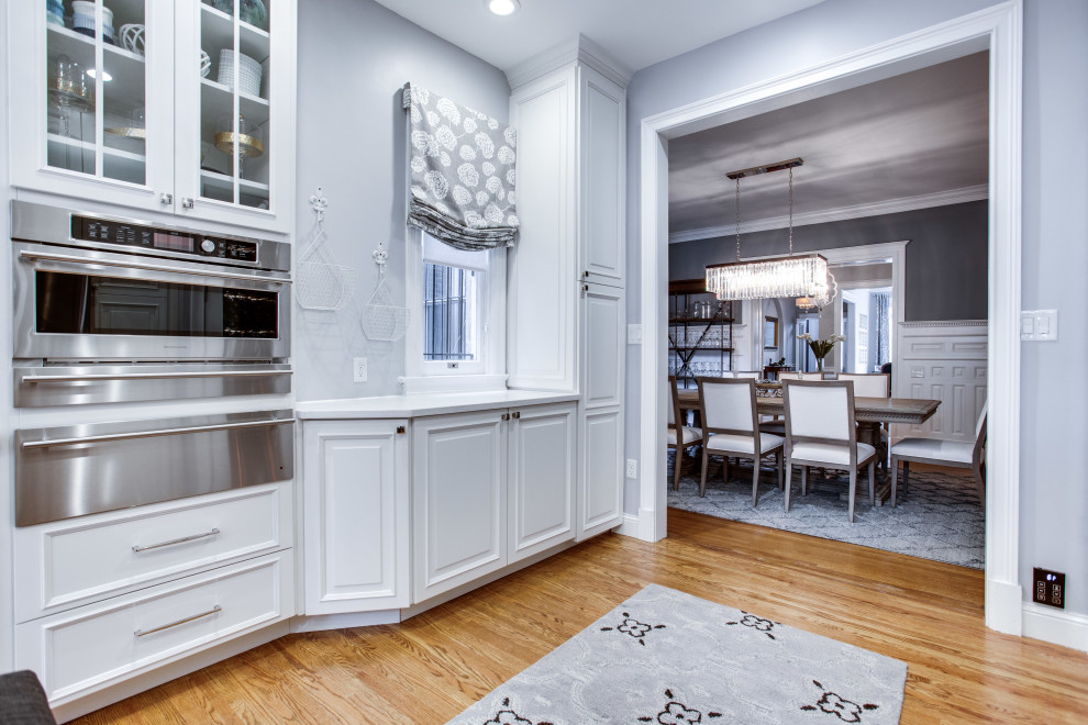 Design ideas for a mid-sized transitional galley kitchen in DC Metro with an undermount sink, raised-panel cabinets, white cabinets, quartz benchtops, stainless steel appliances, medium hardwood floors, with island and white benchtop.