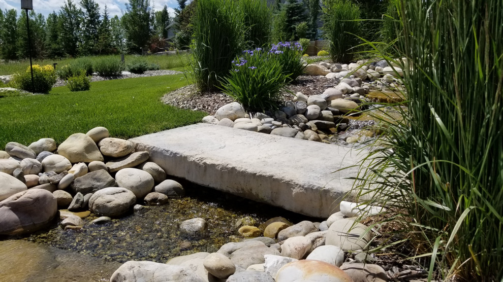 Design ideas for a large transitional backyard full sun formal garden for spring in Calgary with with waterfall and river rock.