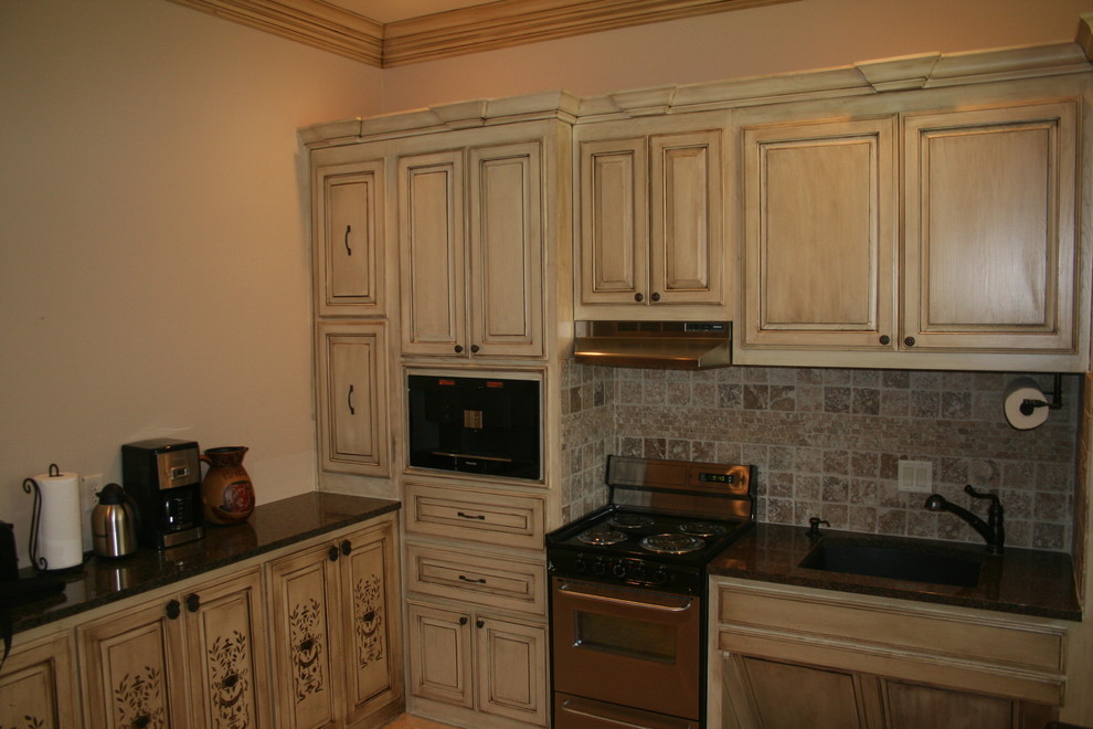 Mid-sized mountain style l-shaped open concept kitchen photo in Dallas with an undermount sink, raised-panel cabinets, light wood cabinets, granite countertops, beige backsplash, limestone backsplash, stainless steel appliances, no island and black countertops