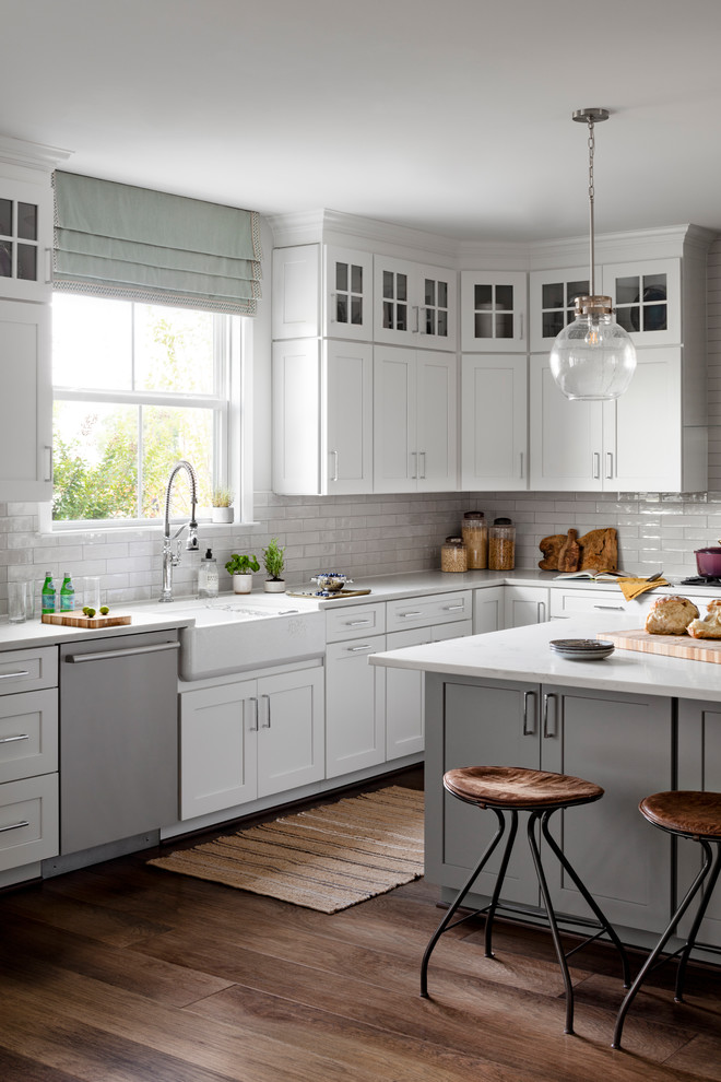 Design ideas for a large country eat-in kitchen in DC Metro with a farmhouse sink, white cabinets, quartz benchtops, white splashback, subway tile splashback, stainless steel appliances, dark hardwood floors, with island, brown floor, white benchtop and shaker cabinets.