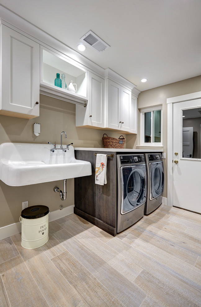Photo of a mid-sized country laundry room in Sacramento with an utility sink, recessed-panel cabinets, white cabinets, quartz benchtops, beige walls, porcelain floors, a side-by-side washer and dryer and beige floor.