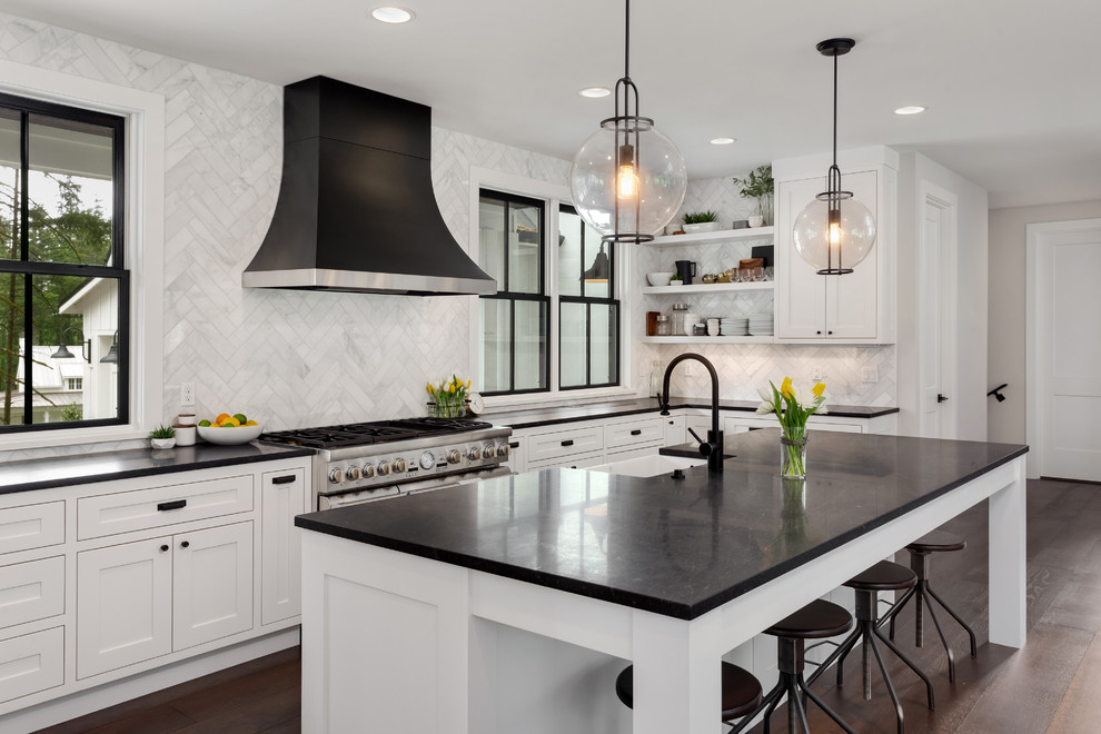 Inspiration for a transitional l-shaped kitchen in San Francisco with a farmhouse sink, shaker cabinets, white cabinets, white splashback, dark hardwood floors, with island, brown floor and black benchtop.