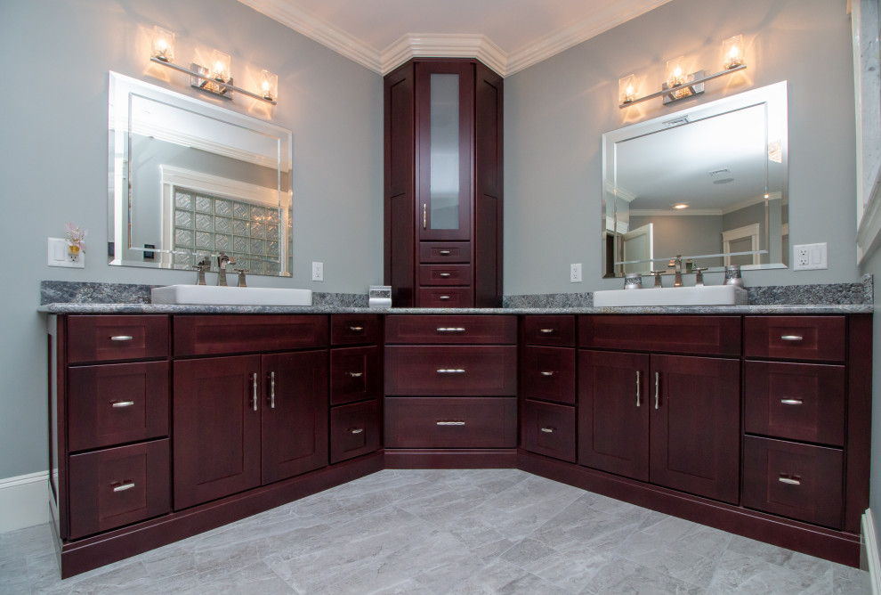Photo of a large transitional master bathroom in Manchester with recessed-panel cabinets, medium wood cabinets, a drop-in tub, a corner shower, a two-piece toilet, multi-coloured tile, porcelain tile, grey walls, porcelain floors, a drop-in sink, granite benchtops, grey floor, a hinged shower door, multi-coloured benchtops, a shower seat, a double vanity and a freestanding vanity.