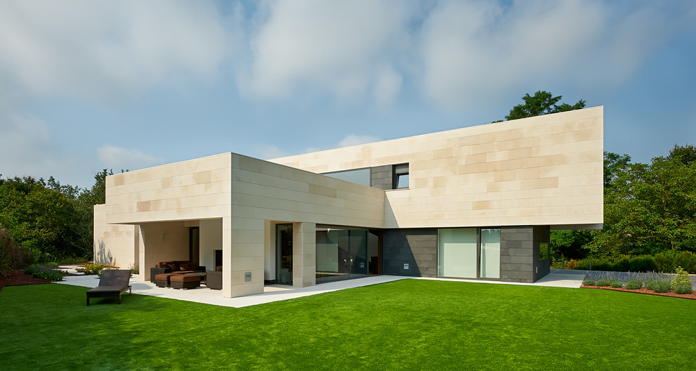 This is an example of a large contemporary two-storey beige exterior in Other with a flat roof and stone veneer.