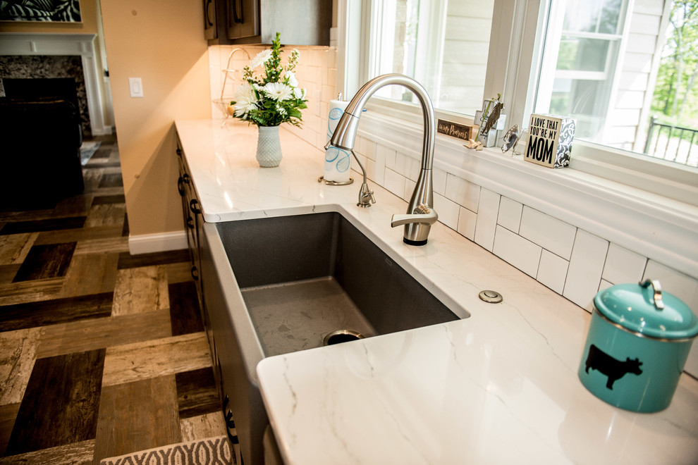 Example of a large transitional l-shaped vinyl floor and multicolored floor open concept kitchen design with a farmhouse sink, shaker cabinets, gray cabinets, quartz countertops, white backsplash, subway tile backsplash, stainless steel appliances, an island and white countertops