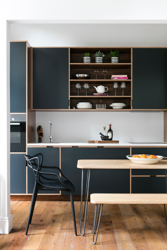 Contemporary single-wall kitchen in London with flat-panel cabinets, blue cabinets, solid surface benchtops, white splashback, panelled appliances and medium hardwood floors.