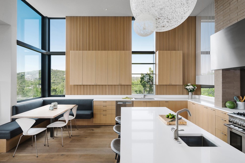 This is an example of a contemporary l-shaped kitchen in Austin with an undermount sink, flat-panel cabinets, light wood cabinets, stainless steel appliances, light hardwood floors, with island, beige floor and white benchtop.