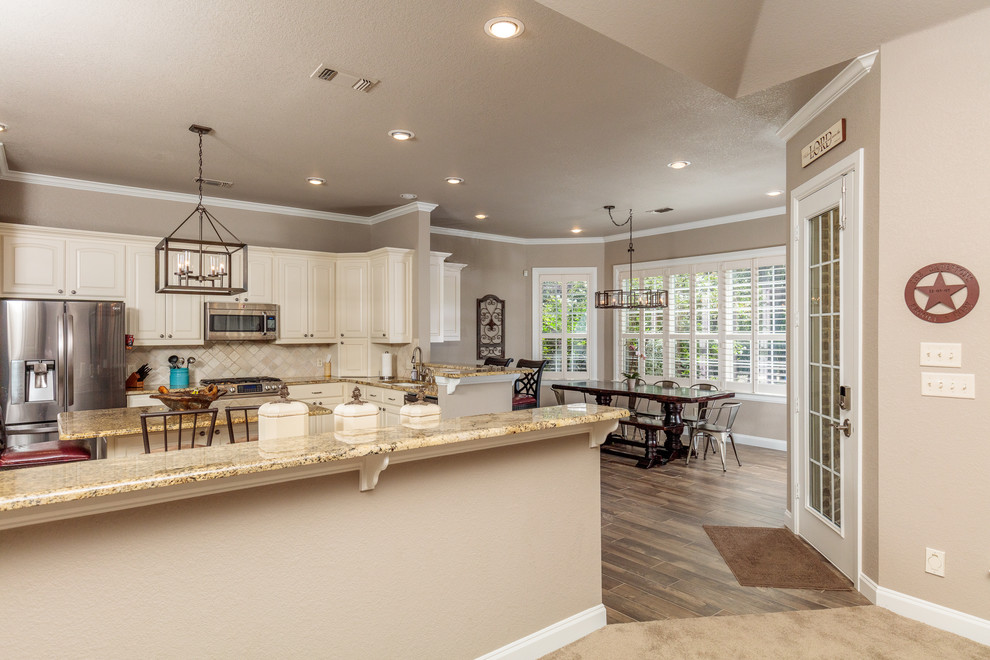 Photo of a large country galley eat-in kitchen in Dallas with raised-panel cabinets, white cabinets, granite benchtops, beige splashback, carpet, with island and brown floor.