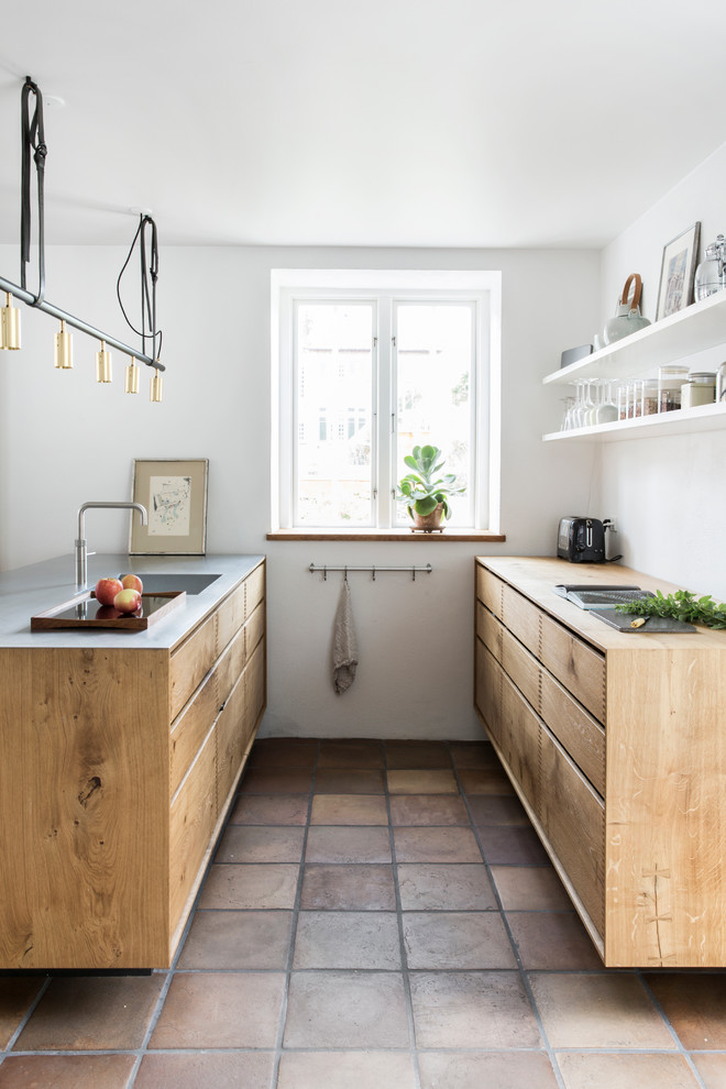 This is an example of a scandinavian kitchen in Copenhagen with flat-panel cabinets, white splashback, a peninsula and terra-cotta floors.
